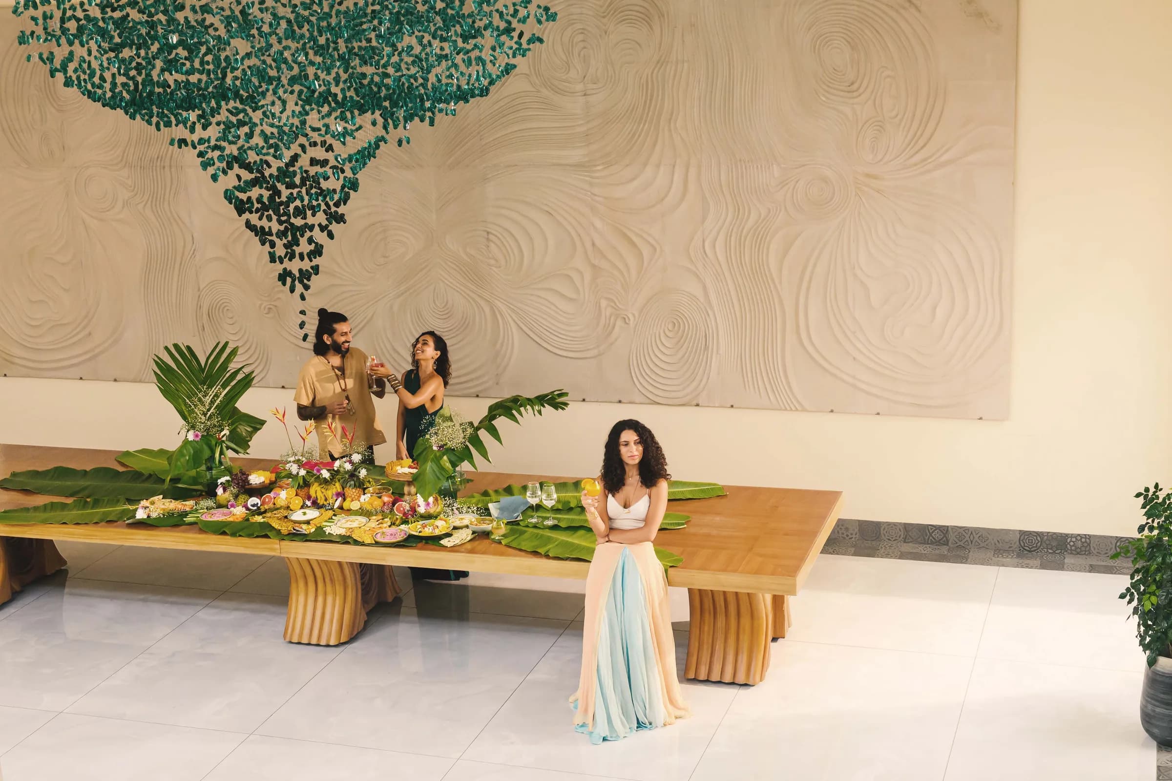 A long dining table beneath a green hanging installation