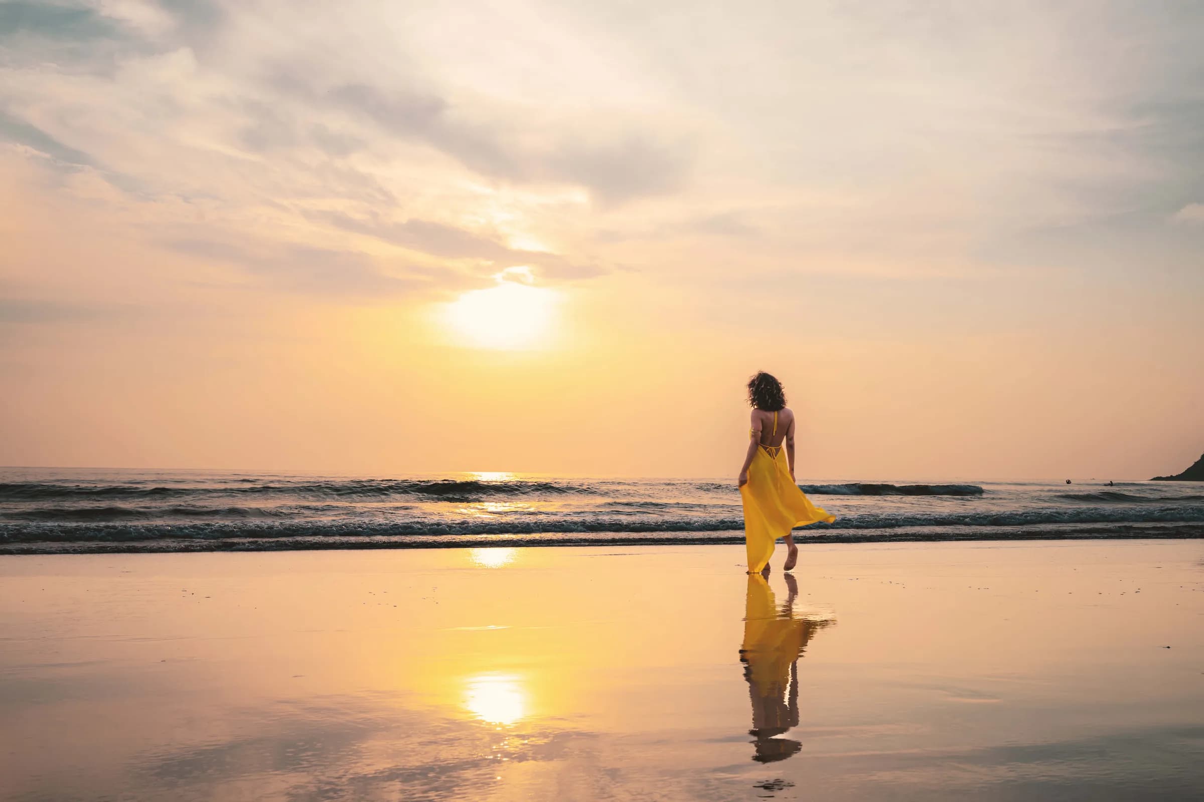 A person walking along the shoreline at sunset
