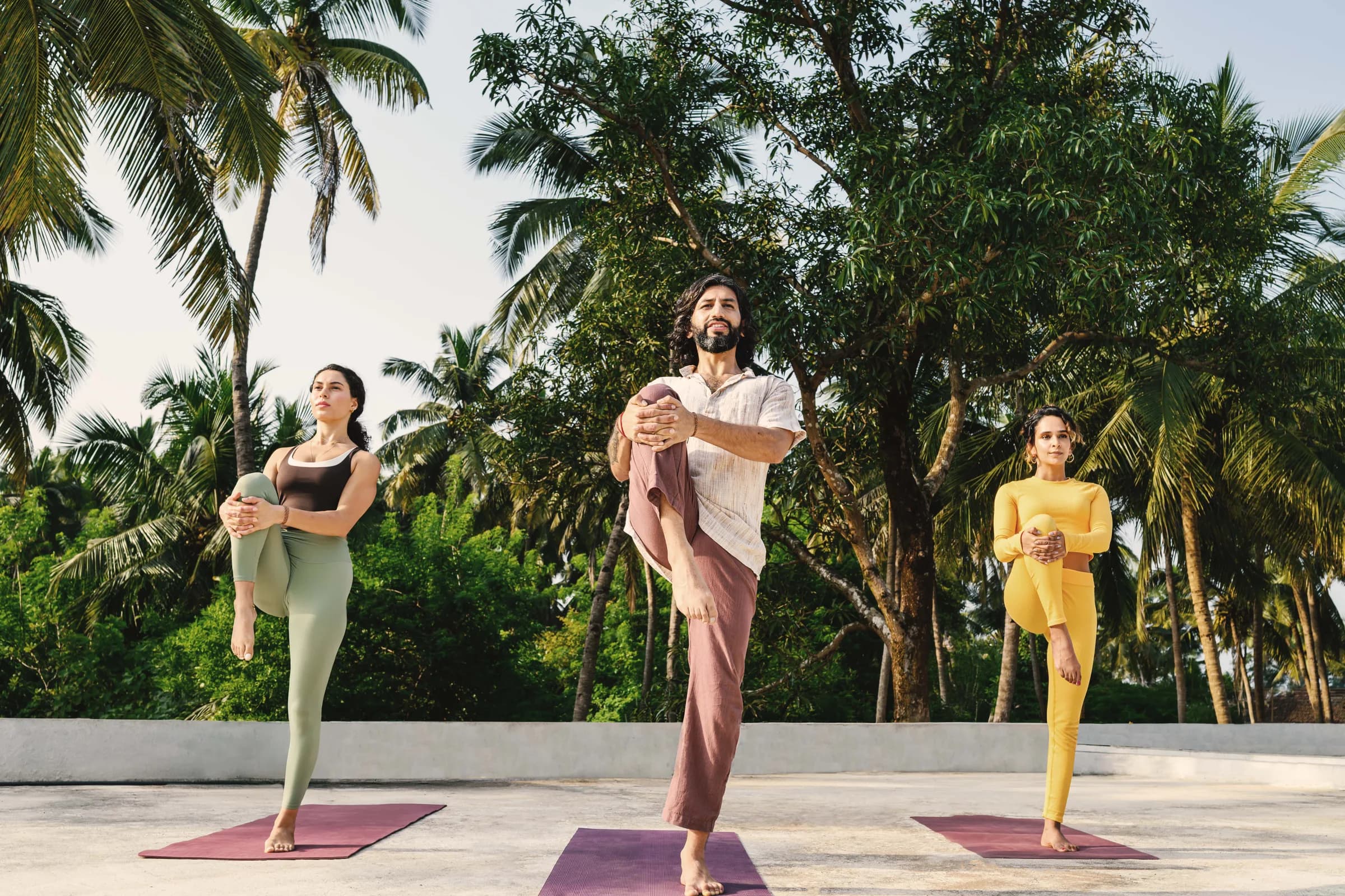 Three people practising standing poses on an open terrace
